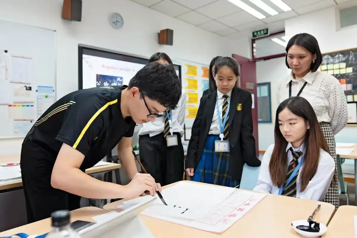 A group of junior school pupils learn calligraphy from a senior school pupil doing a demonstration, highlighting hands-on learning and cultural exploration at Wellington College International Tianjin, a top international school in Tianjin, China.